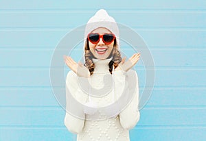 Happy smiling woman having fun wearing a heart shape sunglasses, knitted hat, sweater over blue