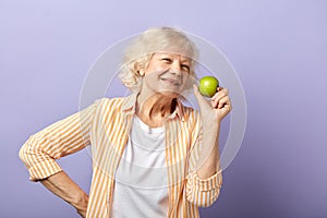 Happy smiling woman in her sixties holding green apple and smiling at camera.