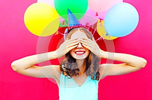 Happy smiling woman is hides her eyes with hands having fun over an air colorful balloons pink