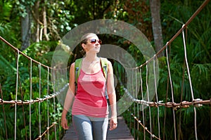 Happy smiling woman hiker crossing suspension bridge in sunlight