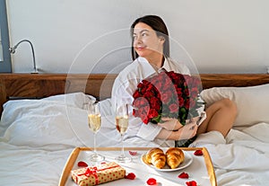 Happy smiling woman holding bouquet of flowers having surprise gift and romantic breakfast in bed