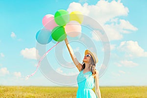 Happy smiling woman holds an air colorful balloons is enjoying a summer day on meadow blue sky