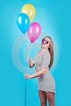 Happy smiling woman is looking on an air colorful balloons having fun over a blue background