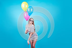 Happy smiling woman is looking on an air colorful balloons having fun over a blue background