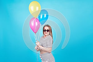 Happy smiling woman is looking on an air colorful balloons having fun over a blue background