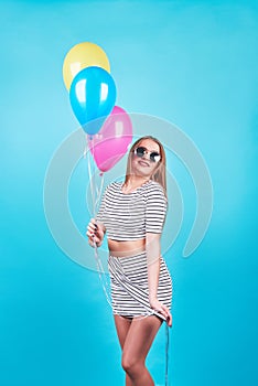 Happy smiling woman is looking on an air colorful balloons having fun over a blue background