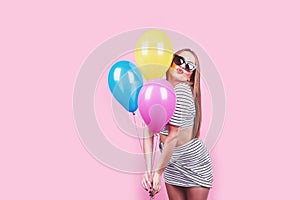 Happy smiling woman is looking on an air colorful balloons having fun over a pink background