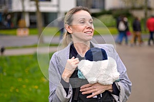 Happy smiling woman looking into the distance while holding and carrying her baby in a baby carrier