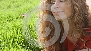 Happy smiling woman lying on green grass enjoying life, young female having fun outdoors in spring park.