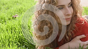 Happy smiling woman lying on green grass enjoying life, young female having fun outdoors in spring park.