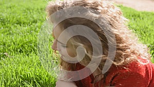 Happy smiling woman lying on green grass enjoying life, young female having fun outdoors in spring park.