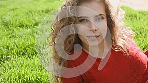 Happy smiling woman lying on green grass enjoying life, young female having fun outdoors in spring park.