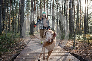 Happy smiling woman pet lover run on wooden path in scandinavian pine forest while playing with dog