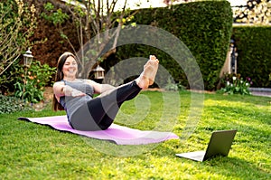 Happy smiling woman practicing pilates lesson online in garden outdoors during quarantine.