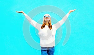 Happy smiling woman raises her hands up wearing white knitted sweater