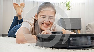 Happy smiling woman rejoicing at her new robot vacuum cleaner doing housework and cleaning dust at home