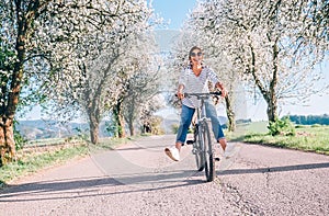 Happy smiling woman rides a bicycle on the country road under the apple blossom trees