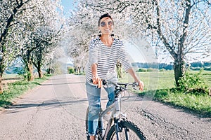 Happy smiling woman rides a bicycle on the country road under blossom trees. Spring is comming concept image photo