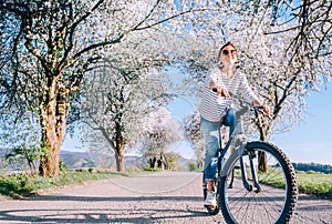 Happy smiling woman rides a bicycle on the country road under blossom trees. Spring is comming concept image