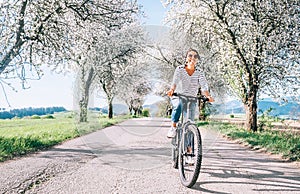 Happy smiling woman rides a bicycle on the country road under blossom trees. Spring is comming concept image