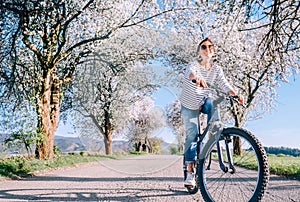 Happy smiling woman rides a bicycle on the country road under blossom trees. Spring is comming concept image photo