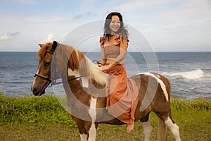 Happy smiling woman riding horse near the ocean. Outdoor activities. Traveling concept. Bali