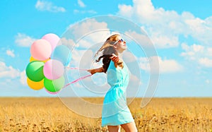 Happy smiling woman running with an air colorful balloons enjoying a summer day on field and blue sky background