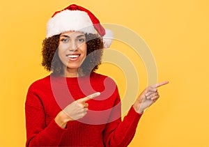 Happy smiling woman in santa claus hat pointing finger at copy space on yellow background, Christmas, xmas concept