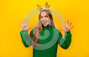 Happy smiling woman shows delight or number ten and wears sweater with Christmas reindeer antlers on yellow background.