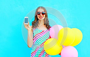 Happy smiling woman shows smartphone holding an air colorful balloons