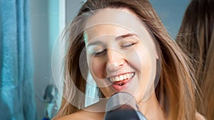 Happy smiling woman singing with hair dryer at bathroom