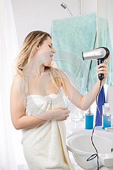 Happy smiling woman singing in hairdryer after having bath and washing ahir