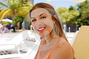 Happy smiling woman sitting on deck chair in tropical pool. Laughing girl enjoying the sun on holidays at hotel resort beach while