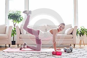 Happy smiling woman in sportswear doing fitness donkey kicks exercise and having fun at home