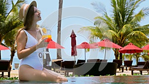 Happy smiling woman in swimwear sitting on pool edge, relax and sunbathing