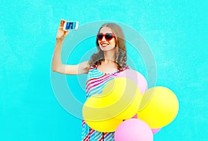 Happy smiling woman taking a picture on a smartphone with an air colorful balloons