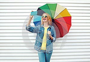 Happy smiling woman taking selfie picture by phone with colorful umbrella in city on white wall