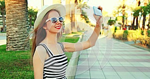 Happy smiling woman taking selfie picture by smartphone over palm tree