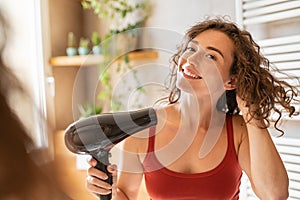 Happy smiling woman using hair dryer in bathroom