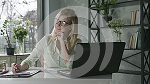 Happy smiling woman working at computer in to office with fresh flowers, rejoicing for success young business woman used