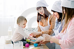 Happy smiling women baking together with little baby girl at home kitchen, Mothers Day, Family concept. Women are