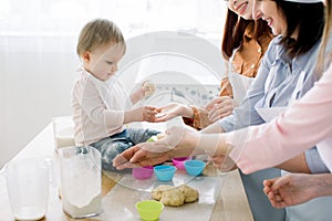 Happy smiling women baking together with little baby girl at home kitchen, Mothers Day, Family concept. Women are
