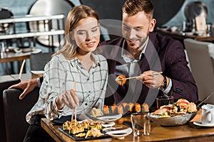 Happy smiling young adult couple eating sushi rolls