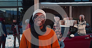 Happy smiling young African American man in winter hat, eyeglasses smiling at camera at fun Christmas party slow motion.