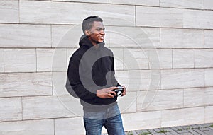 Happy smiling young african man with vintage film camera in black hoodie walking on city street