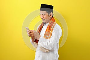 Happy Smiling Young Asian Muslim man wearing moslim clothes holding mobile phone look at phone screen