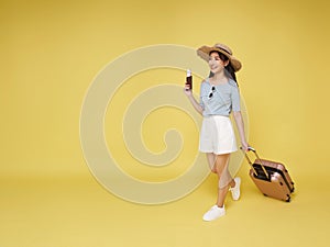 Happy smiling young Asian tourist woman holding passport ticket and luggage going to travel on summer holidays isolated on yellow