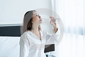 Happy smiling young Asian woman drinking water after waking up in the morning. Healthy, beauty, diet concept