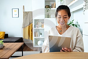 Happy and smiling young Asian woman working at home office holding tablet reading document. Social media.