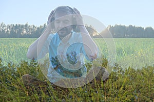 Happy smiling young bearded man sitting wearing headphones and listen to relaxation music on nature on sunset. Double exposure.